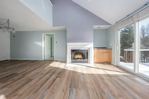 a view of an empty room with wooden floor fireplace and a window