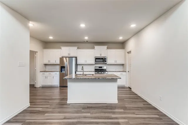 a large kitchen with stainless steel appliances kitchen island a stove a sink dishwasher a refrigerator and white cabinets with wooden floor