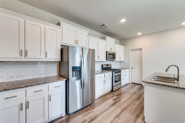 a kitchen with granite countertop a refrigerator stove and sink with wooden floor
