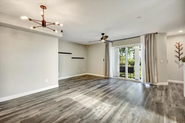 a view of an empty room with wooden floor ceiling fan