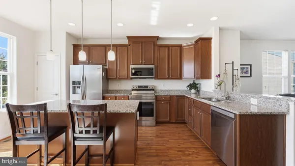 a kitchen with stainless steel appliances granite countertop wooden cabinets a refrigerator a sink a stove a dining table and chairs