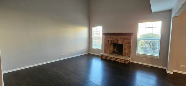an empty room with wooden floor fireplace and windows