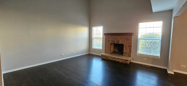 an empty room with wooden floor fireplace and windows