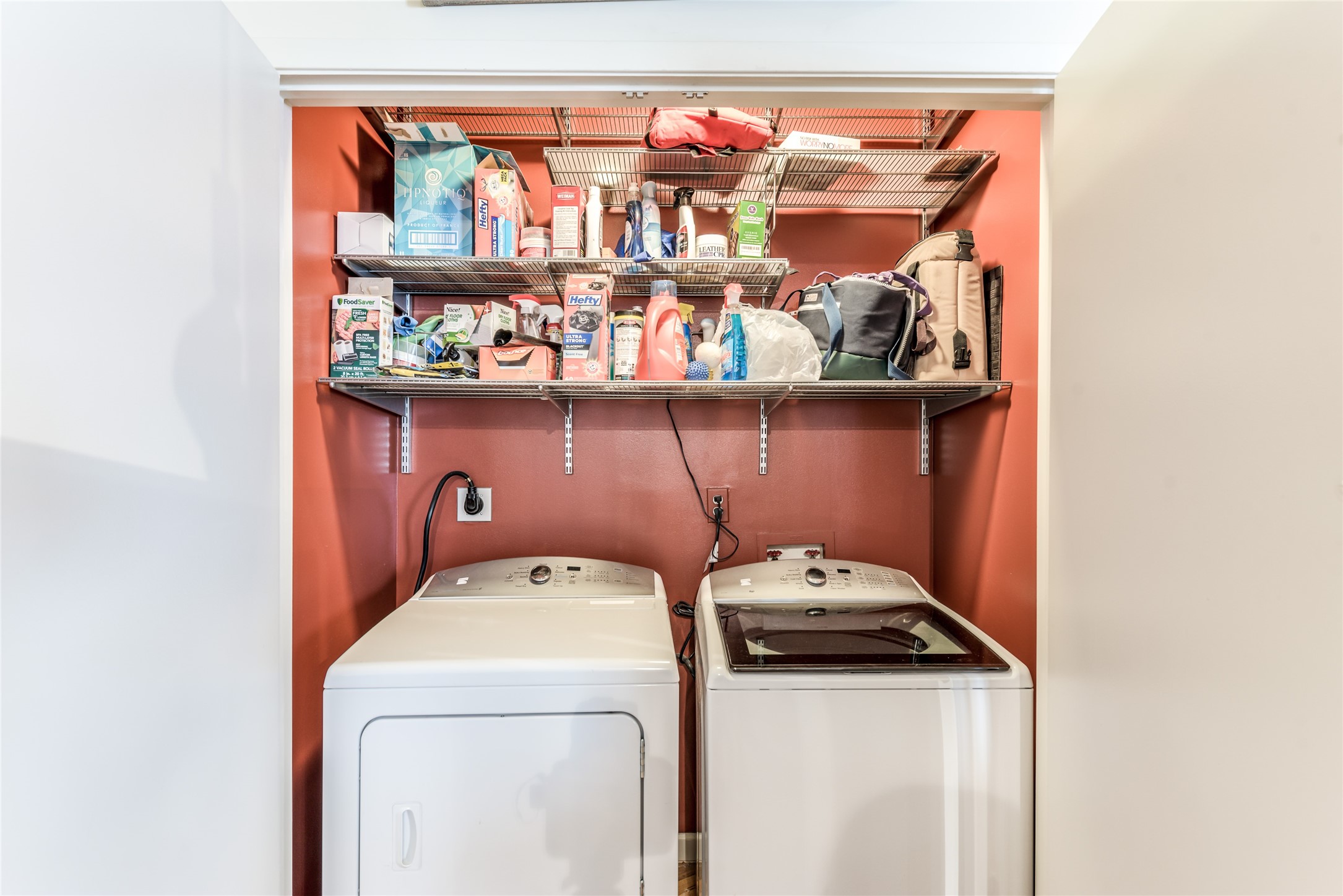 705 Main Street, Unit 215 Houston, TX 77002 - Photo 12 of 36 Compact laundry nook with a washer and dryer below two shelves stocked with various household supplies. Ideal for efficient use of space.