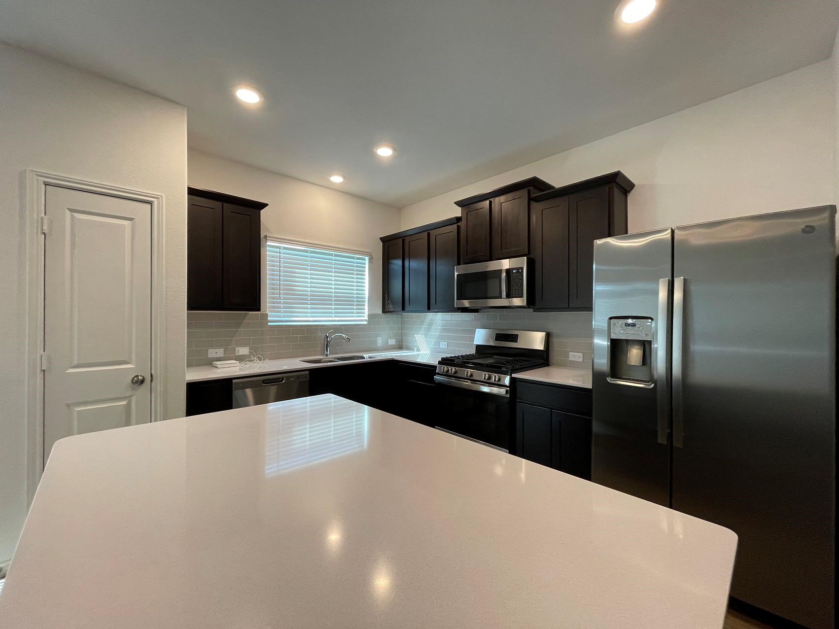 1625 Woolsey Way Leander, TX 78641 - Photo 3 of 17 The kitchen features dark wood cabinetry, stainless steel appliances, a white countertop, and a tiled backsplash