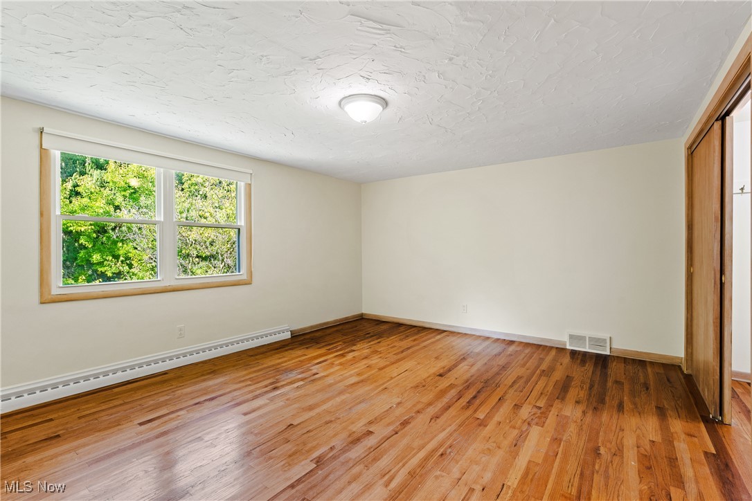 870 Trebisky Road Cleveland, OH 44121 - Photo 30 of 48 Unfurnished bedroom featuring wood-type flooring, a closet, a baseboard heating unit, and a textured ceiling