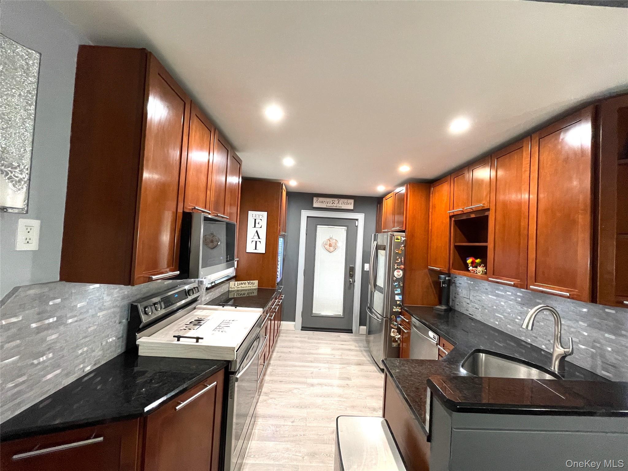 30 Classon Avenue Mastic, NY 11950 - Photo 3 of 21 Kitchen with tasteful backsplash, dark stone countertops, stainless steel appliances, light wood-style floors, and brown cabinets
