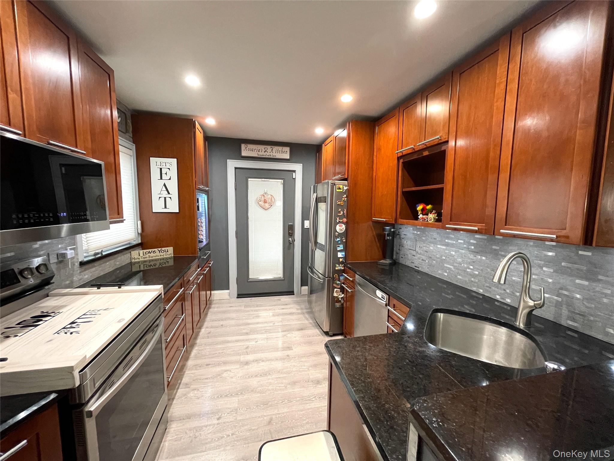 30 Classon Avenue Mastic, NY 11950 - Photo 7 of 21 Kitchen featuring decorative backsplash, appliances with stainless steel finishes, light wood-style floors, dark stone countertops, and open shelves