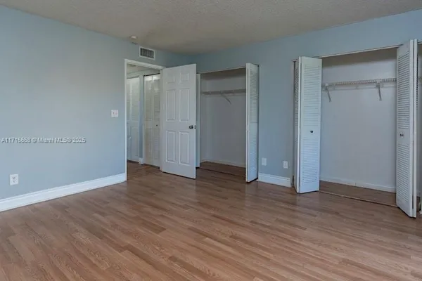 a view of an empty room with wooden floor and closet