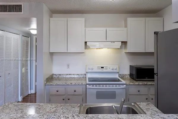 a kitchen with granite countertop a sink a stove and refrigerator