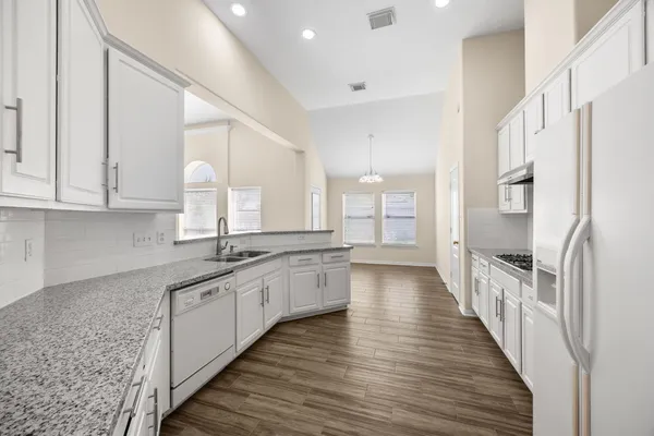 a large white kitchen with stainless steel appliances granite countertop a lot of counter space and wooden floors
