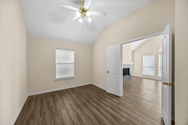 an empty room with wooden floor fan and windows