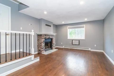 an empty room with wooden floor fireplace and windows