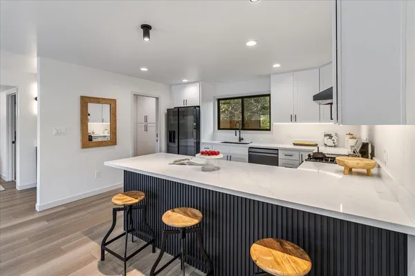 a kitchen with stainless steel appliances granite countertop a refrigerator a sink dishwasher a stove and white cabinets with wooden floor