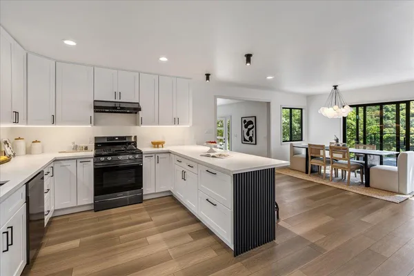 a open kitchen with stainless steel appliances granite countertop a stove top oven a sink dishwasher and a dining table with wooden floor