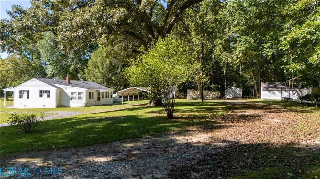 View of green lawn with a carport and view of wooded area