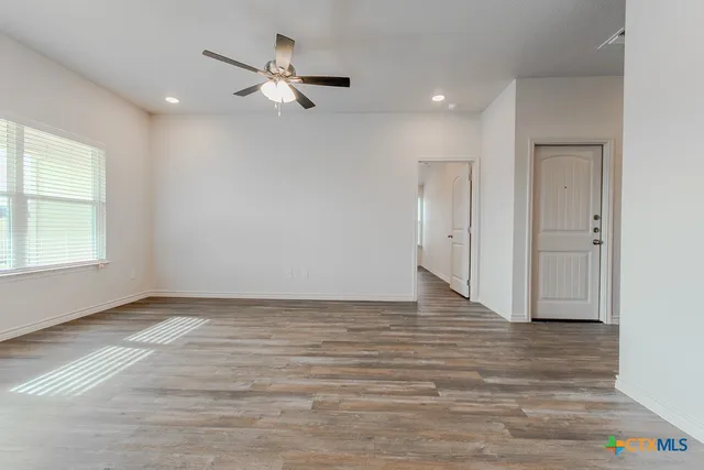a view of an empty room with wooden floor and a ceiling fan