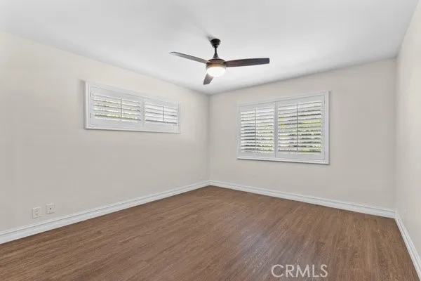 an empty room with wooden floor ceiling fan and windows