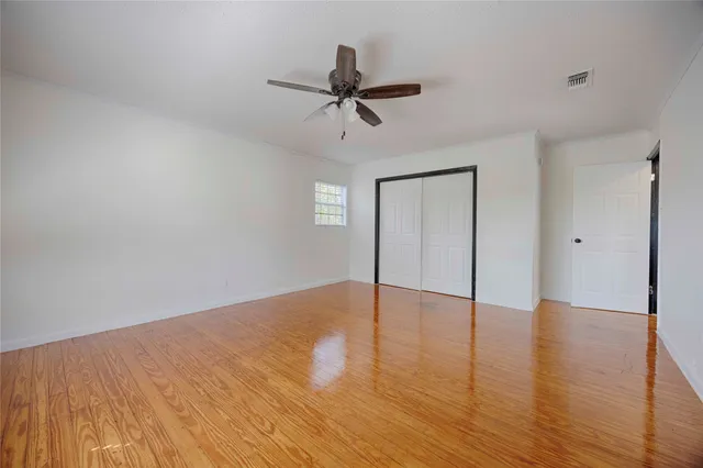a view of an empty room with wooden floor and a ceiling fan