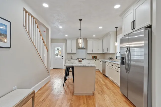 a kitchen with stainless steel appliances a refrigerator a sink dishwasher a stove and white cabinets with wooden floor