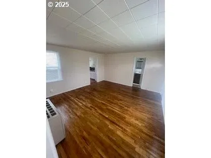 a view of an empty room with wooden floor and a window