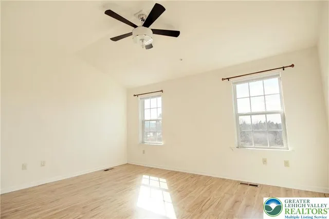 an empty room with wooden floor fan and windows