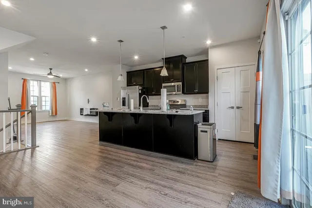 a kitchen with stainless steel appliances kitchen island granite countertop a stove a refrigerator a sink a oven with wooden floor and cabinets