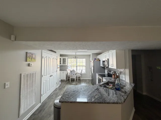 a kitchen with stainless steel appliances granite countertop a stove top oven a sink dishwasher a dining table and chairs with wooden floor