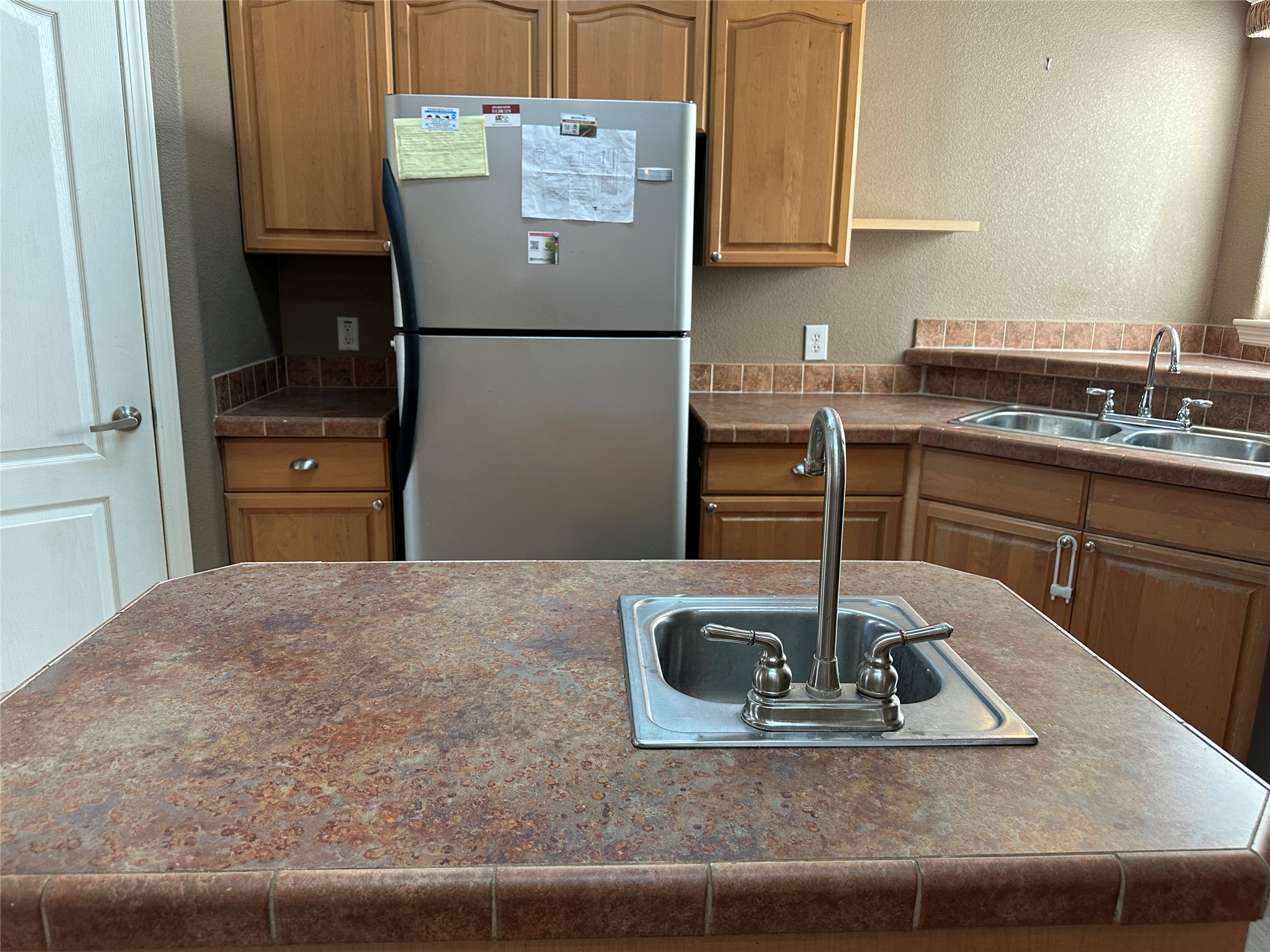 438 Mt Olive Road, Unit A Cedar Creek, TX 78612 - Photo 7 of 27 Kitchen with a textured wall, freestanding refrigerator, dark countertops, a kitchen island with sink, and wood finish cabinetry