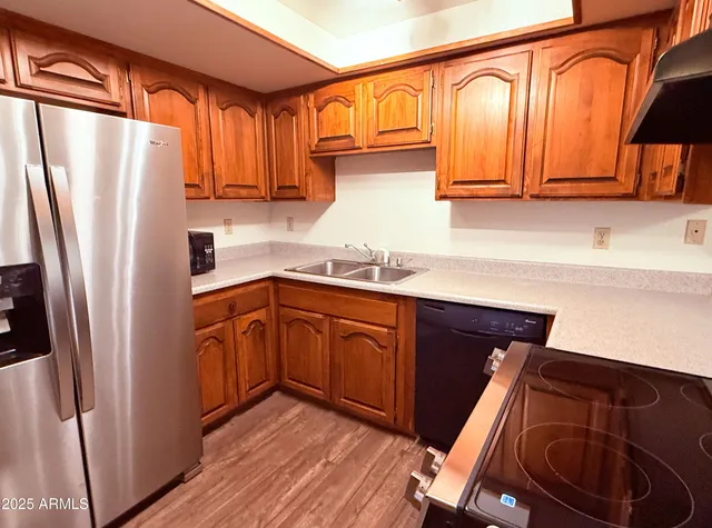 a kitchen with stainless steel appliances granite countertop a refrigerator a sink dishwasher and wooden cabinets with wooden floor