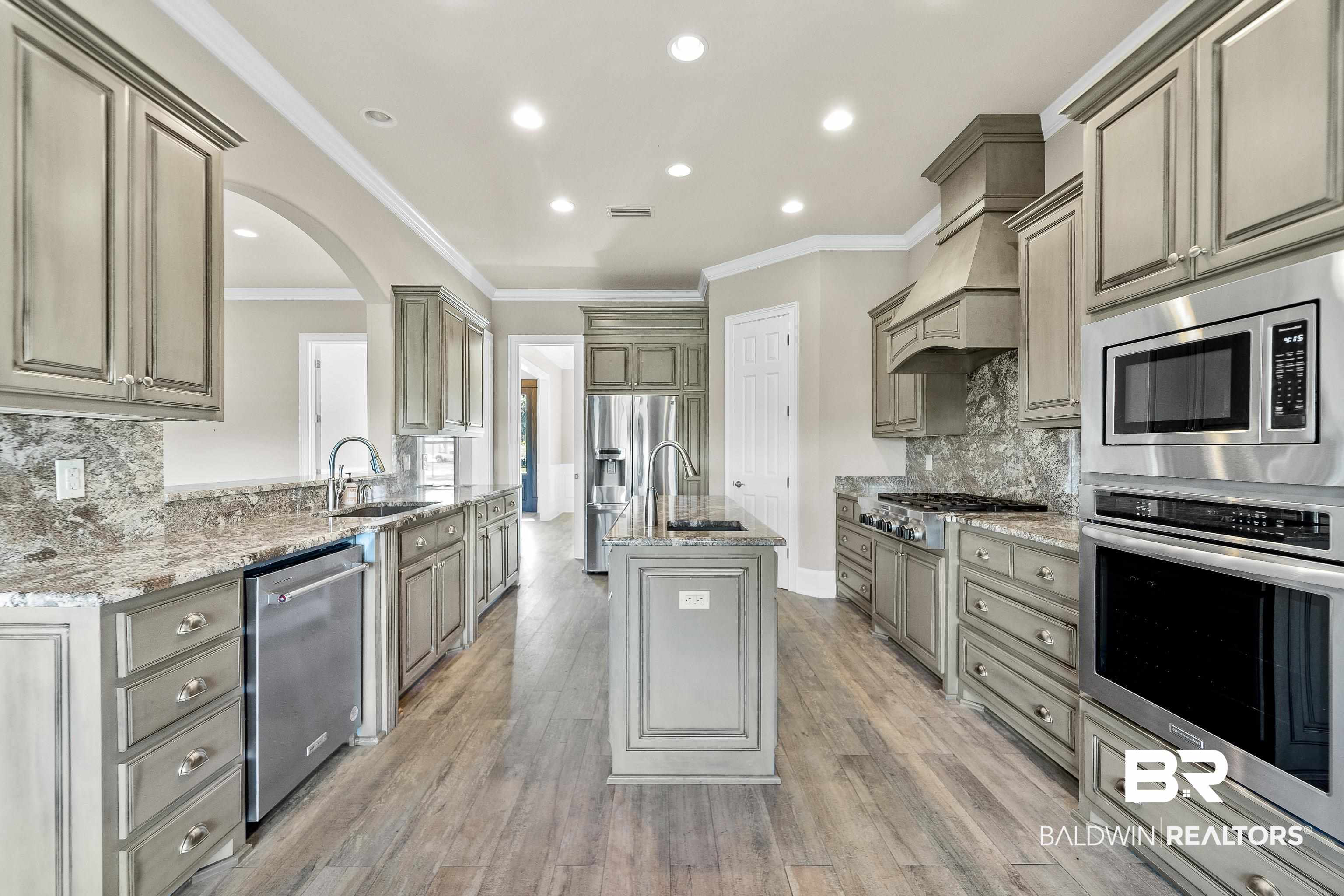 17663 Burwick Loop Fairhope, AL 36532 - Photo 14 of 41 Kitchen featuring appliances with stainless steel finishes, light stone countertops, hardwood / wood-style flooring, a center island with sink, and sink