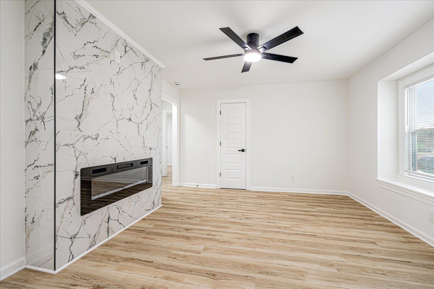 Unfurnished living room featuring a fireplace, light wood-type flooring, heating unit, a ceiling fan, and an accent wall