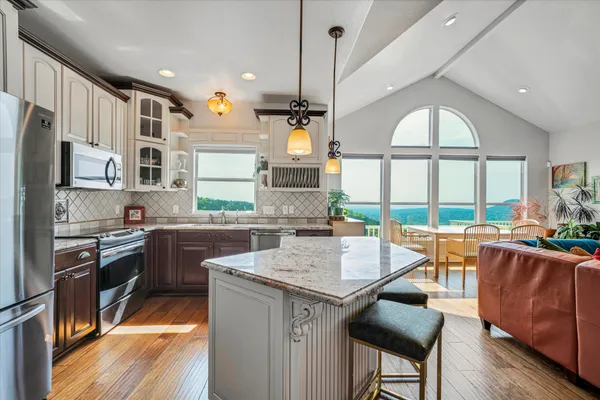 a kitchen with stainless steel appliances granite countertop a stove a refrigerator a sink dishwasher a dining table and chairs with wooden floor