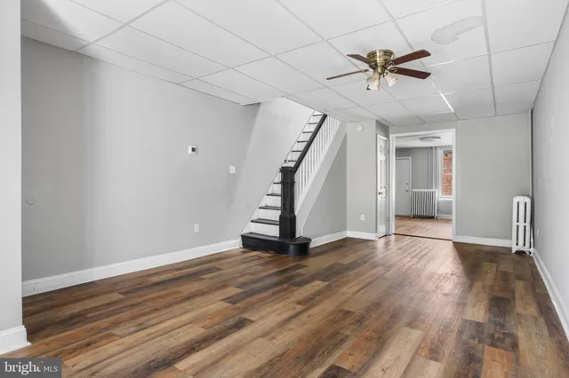 a view of an empty room with wooden floor and a ceiling fan