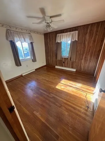 an empty room with wooden floor chandelier fan and windows
