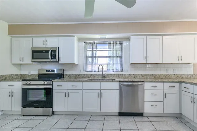 a kitchen with white cabinets appliances a sink and a window