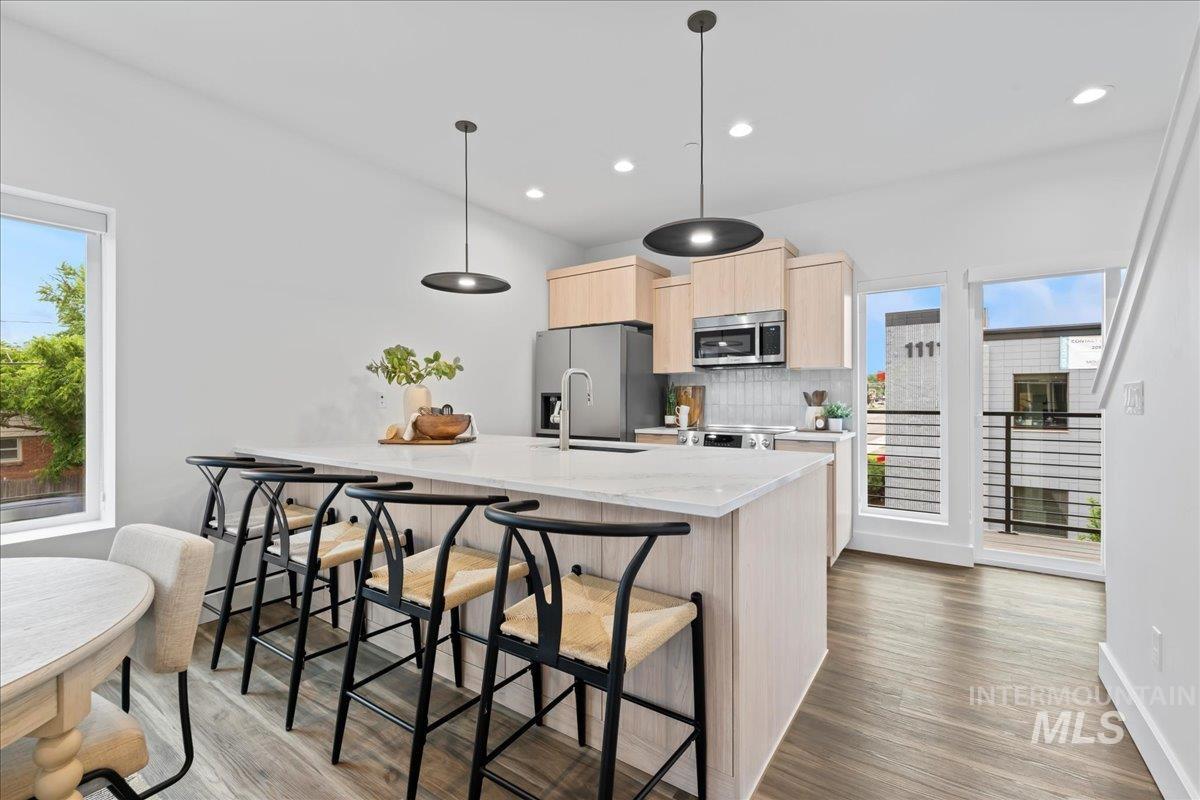 1011 South Orchard Street, Unit 101 Boise, ID 83705 - Photo 2 of 16 Kitchen featuring light brown cabinetry, wood finished floors, a kitchen breakfast bar, appliances with stainless steel finishes, and decorative backsplash