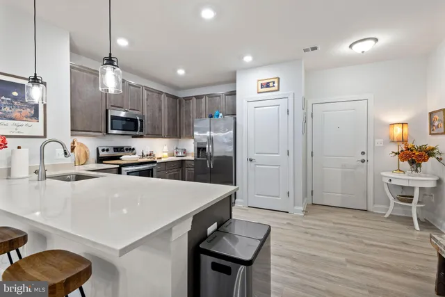 a kitchen with stainless steel appliances a refrigerator a stove a sink a dining table and chairs with wooden floor