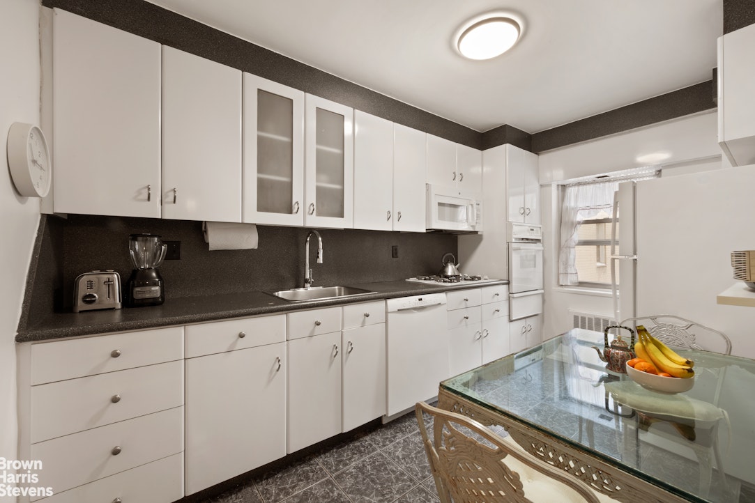 135 East 83rd Street, Unit 7A Manhattan, NY 10028 - Photo 3 of 8 a kitchen with stainless steel appliances granite countertop a sink and white cabinets