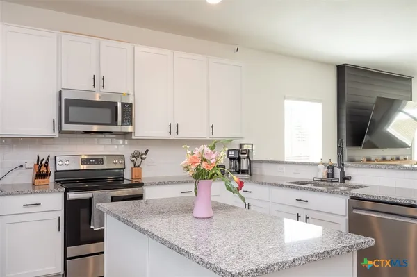 a kitchen with kitchen island granite countertop a sink a stove top oven and cabinetry