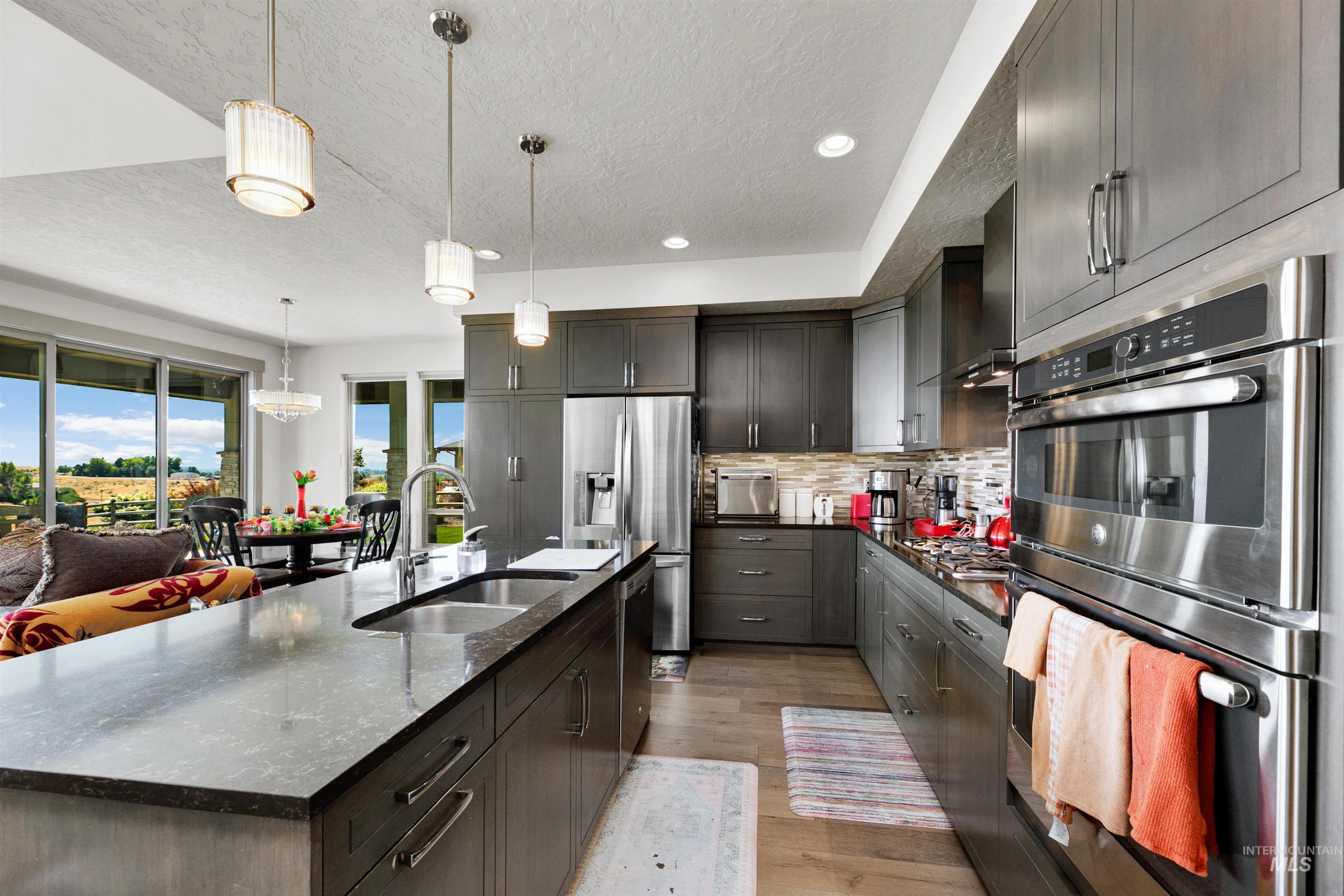 24398 Tombstone Ridge Court Middleton, ID 83644 - Photo 30 of 47 Open-concept kitchen featuring dark wood-finish cabinetry, stainless steel appliances, and a central island with a double basin sink
