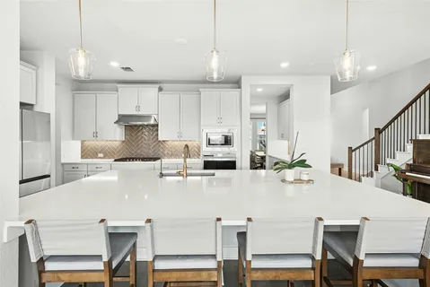 a white kitchen with stainless steel appliances a table chairs and a refrigerator