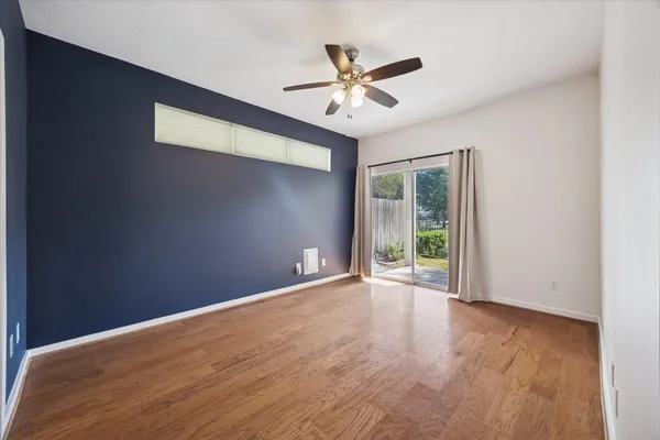 a view of an empty room with wooden floor and a ceiling fan