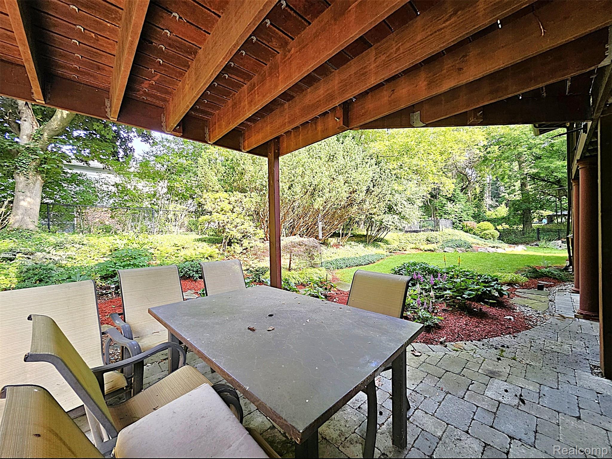 7120 Pebblecreek Road West Bloomfield, MI 48322 - Photo 6 of 31 Covered patio featuring a paver stone surface, wood-beamed ceiling, and a lush landscaped yard with mature plantings and a manicured lawn