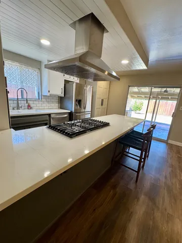 a room with stainless steel appliances granite countertop a stove a sink dishwasher and a dining table with wooden floor