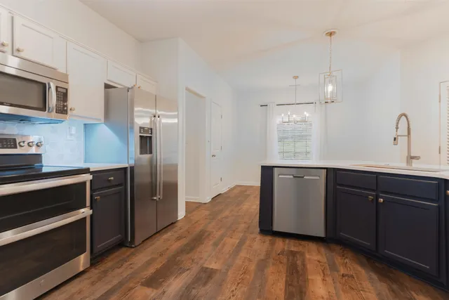 a kitchen with stainless steel appliances granite countertop a refrigerator a sink dishwasher a stove and white cabinets with wooden floor