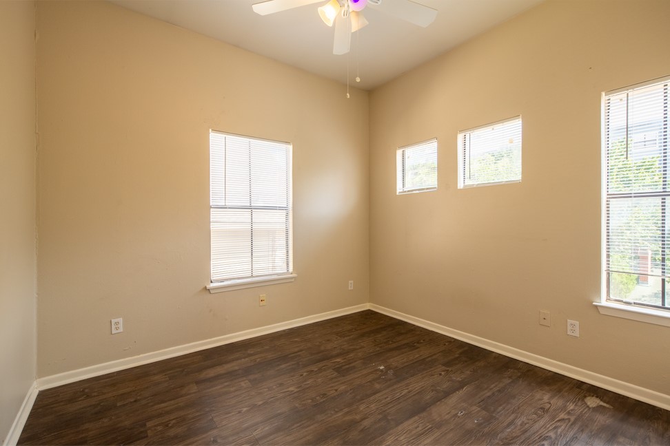 712 Graham Place, Unit 305 Austin, TX 78705 - Photo 10 of 18 Empty room with plenty of natural light, dark wood finished floors, and a ceiling fan