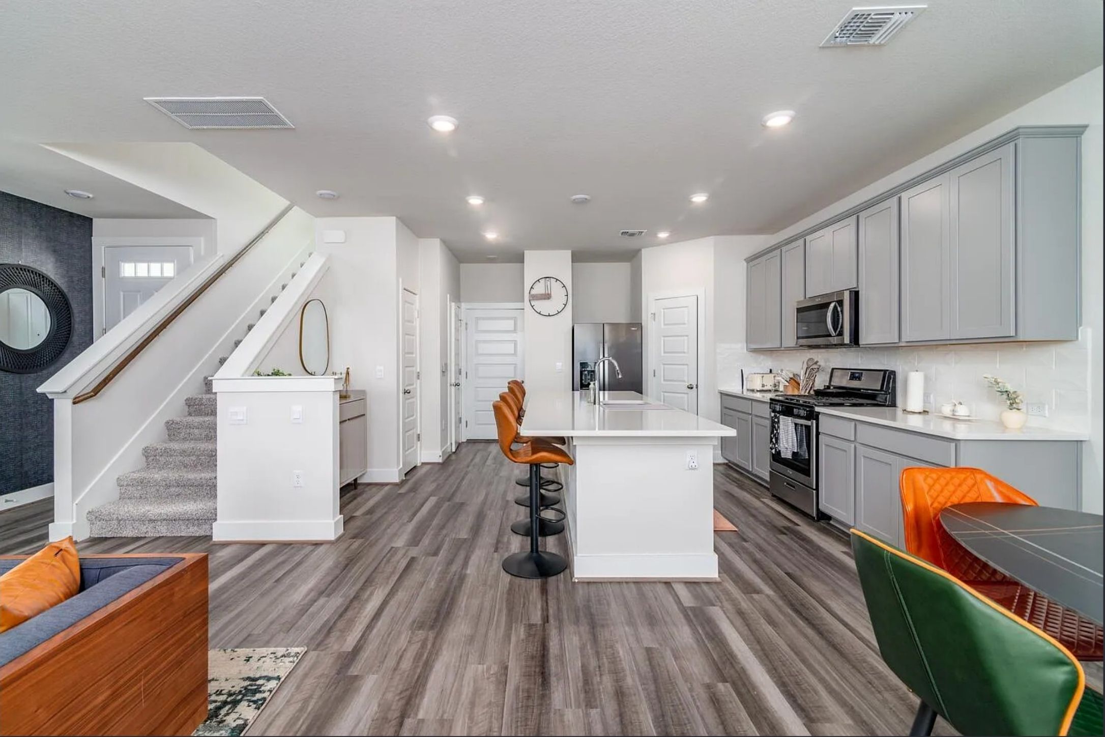 7501 Travertine Spring Drive Austin, TX 78744 - Photo 7 of 28 Open-concept living space featuring wood-finish flooring, a contemporary kitchen with gray cabinetry, an island with seating, stainless steel appliances, and a carpeted staircase with white risers and a wood handrail