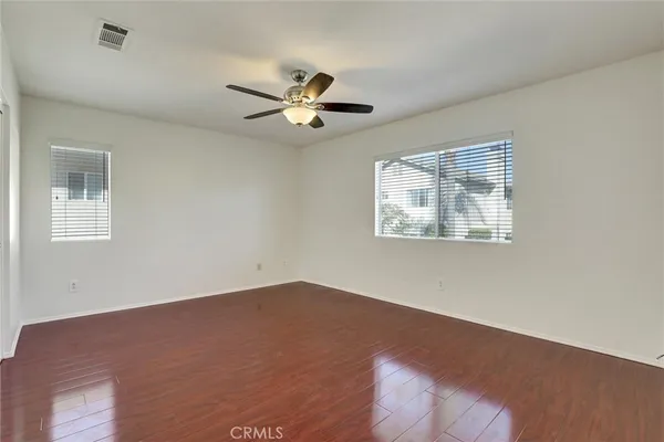 a view of an empty room with wooden floor and a ceiling fan
