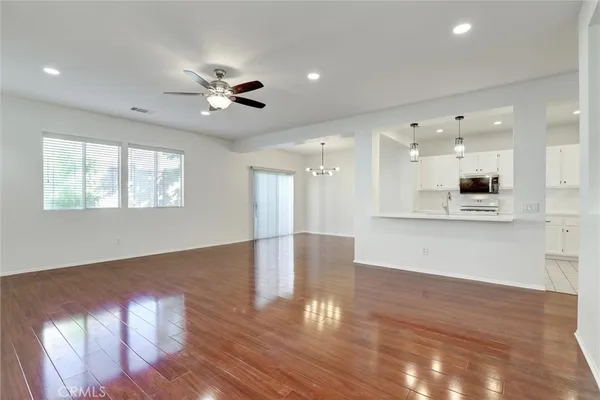 a view of an empty room and kitchen with wooden floor